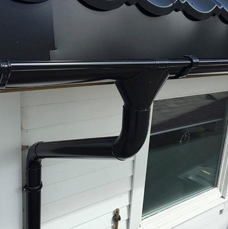 A black gutter and downpipe on the corner of a white house