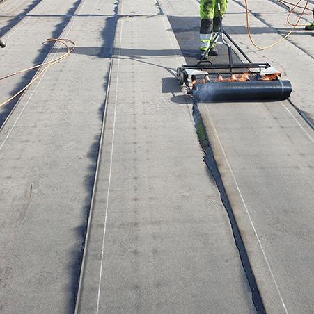 A roofer rolling out a new sheet of membrane on a flat roof