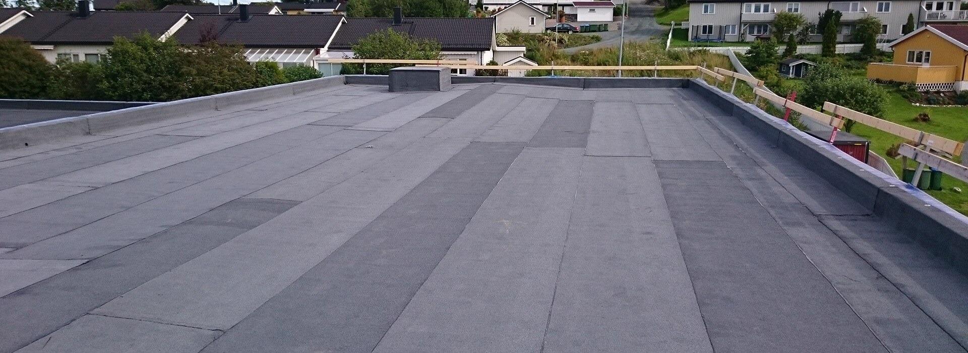 A finished flat roof in dark membrane with a timber railing, houses and trees beyond