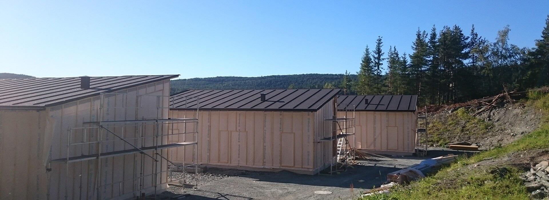 A row of new timber sheds with dark roofs, with forest behind