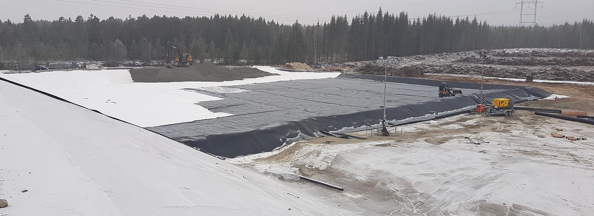 A large flat roof half covered in white membrane, with early snow around the site
