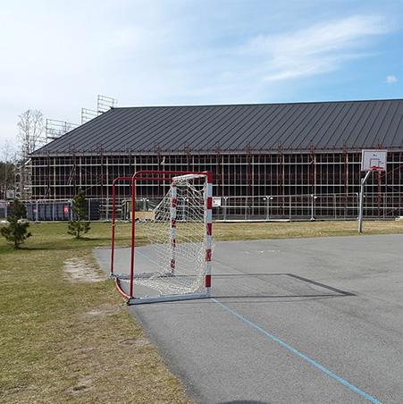 A large hall with scaffolding along its side, behind a football pitch